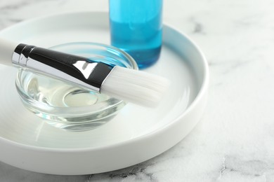 Bowl of chemical peel and brush on white marble table, closeup. Peeling procedure