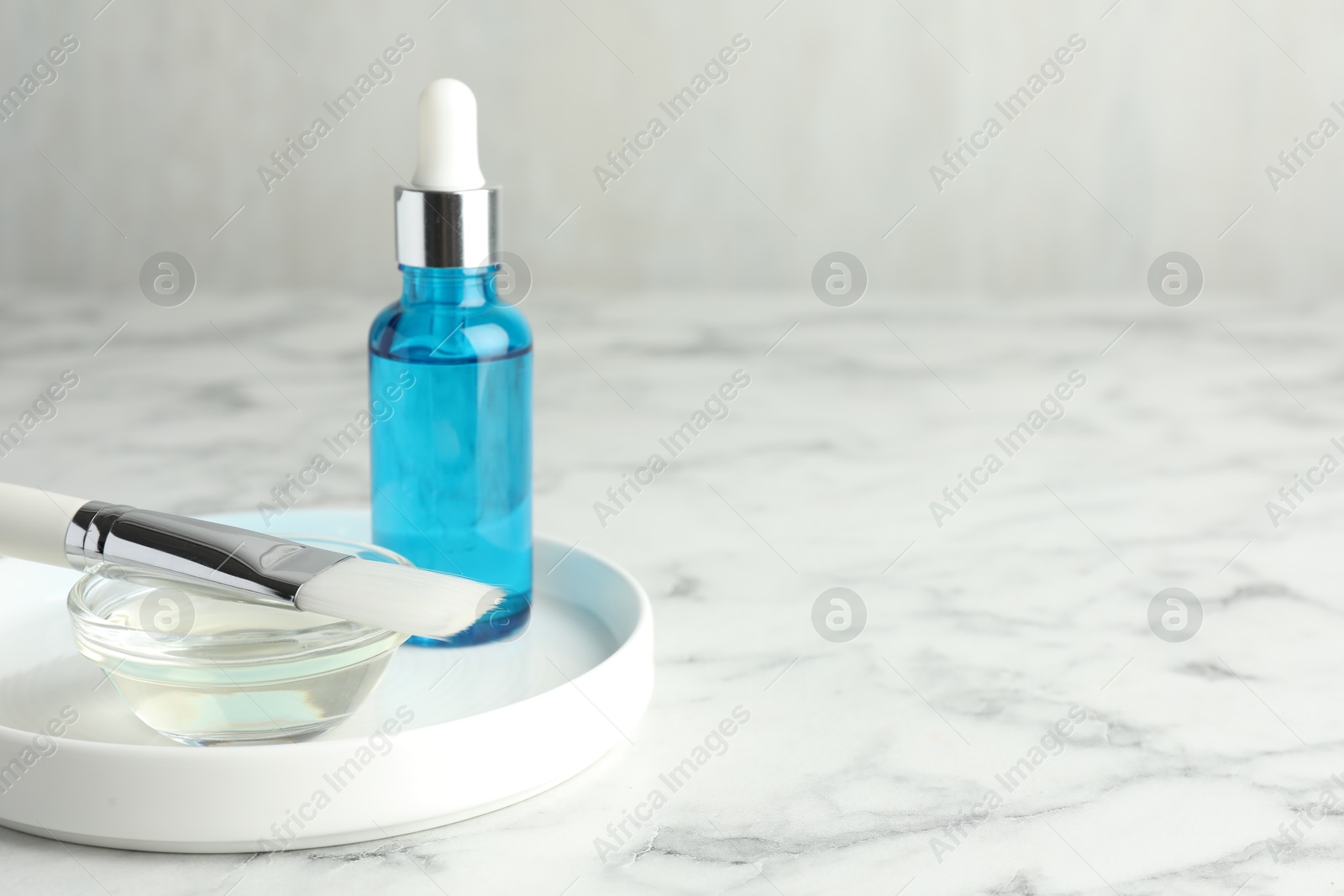 Photo of Bottle of chemical peel, bowl with liquid and brush on white marble table, space for text. Peeling procedure