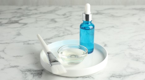 Bottle of chemical peel, bowl with liquid and brush on white marble table. Peeling procedure