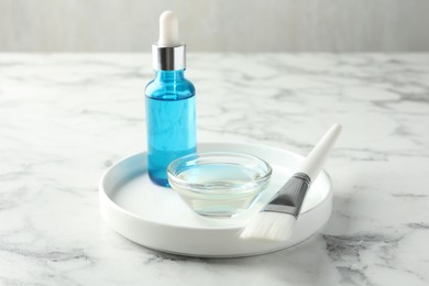 Photo of Bottle of chemical peel, bowl with liquid and brush on white marble table. Peeling procedure