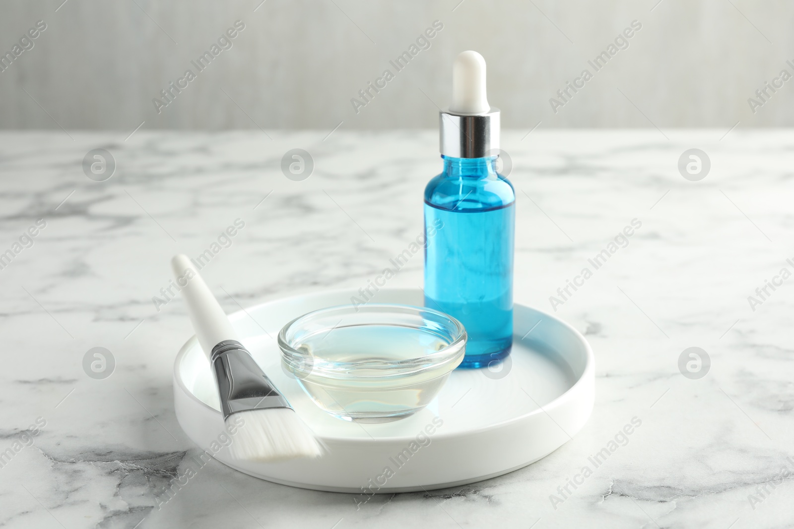 Photo of Bottle of chemical peel, bowl with liquid and brush on white marble table. Peeling procedure