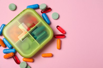 Photo of Different pills and organizer on pink background, flat lay. Space for text