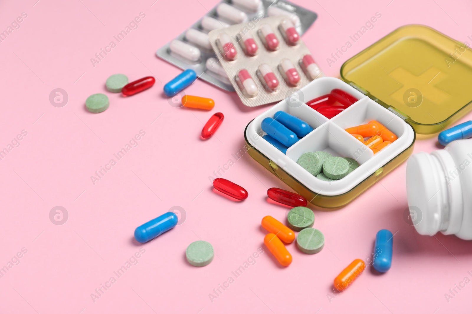 Photo of Different pills, organizer and medical jar on pink background, closeup