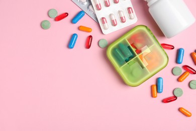 Photo of Different pills, organizer and medical jar on pink background, flat lay. Space for text