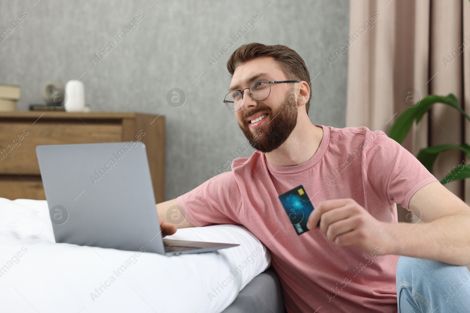 Photo of Online banking. Happy young man with credit card and laptop paying purchase at home