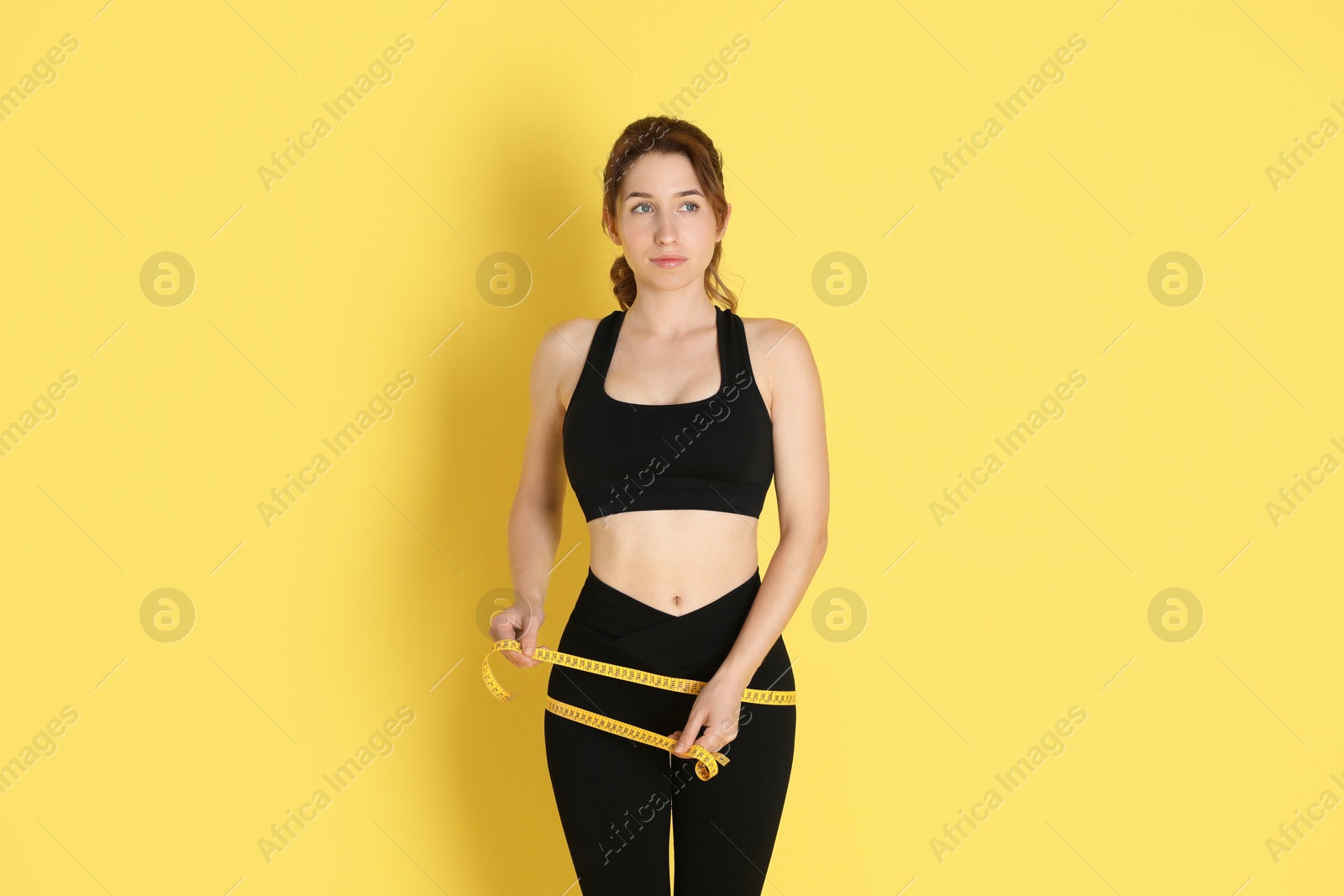 Photo of Woman with measuring tape showing her slim body against yellow background