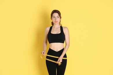 Woman with measuring tape showing her slim body against yellow background