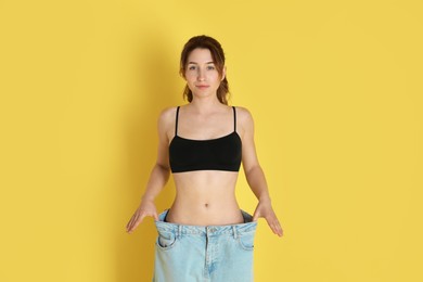 Photo of Woman in big jeans showing her slim body on yellow background, space for text