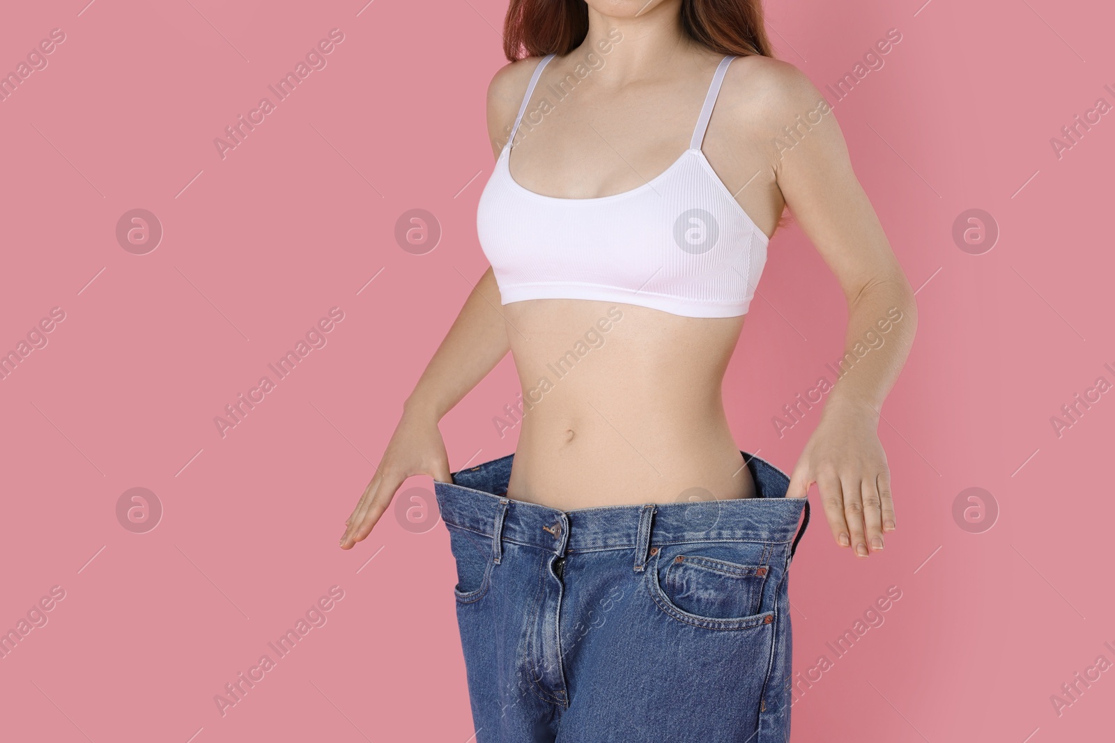 Photo of Woman in big jeans showing her slim body on pink background, closeup. Space for text