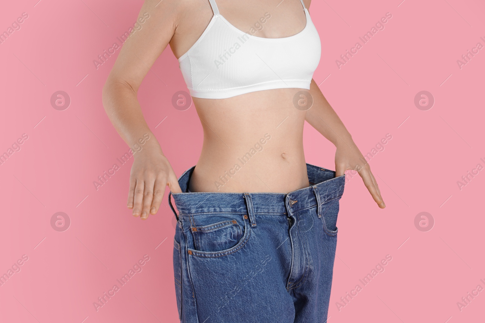 Photo of Woman in big jeans showing her slim body on pink background, closeup