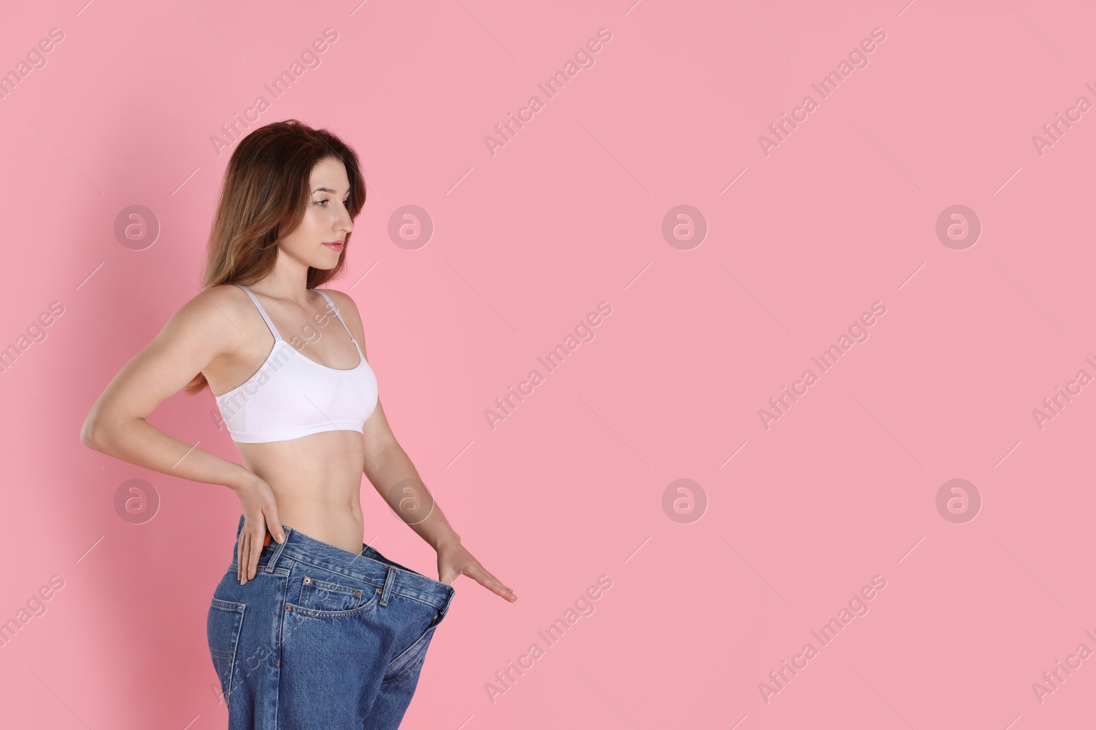 Photo of Woman in big jeans showing her slim body on pink background, space for text