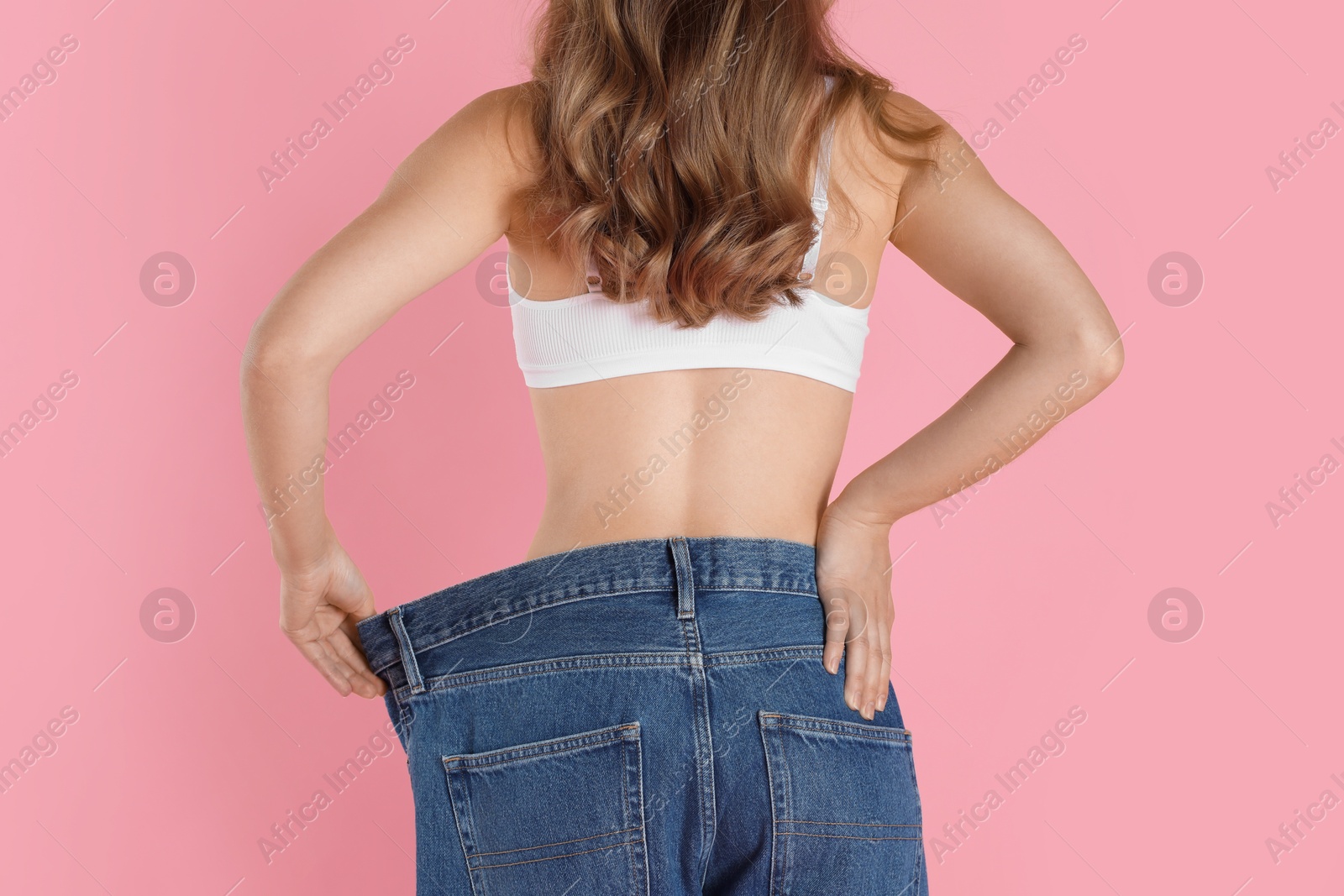 Photo of Woman in big jeans showing her slim body on pink background, closeup