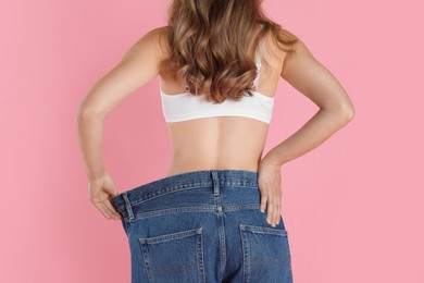 Photo of Woman in big jeans showing her slim body on pink background, closeup