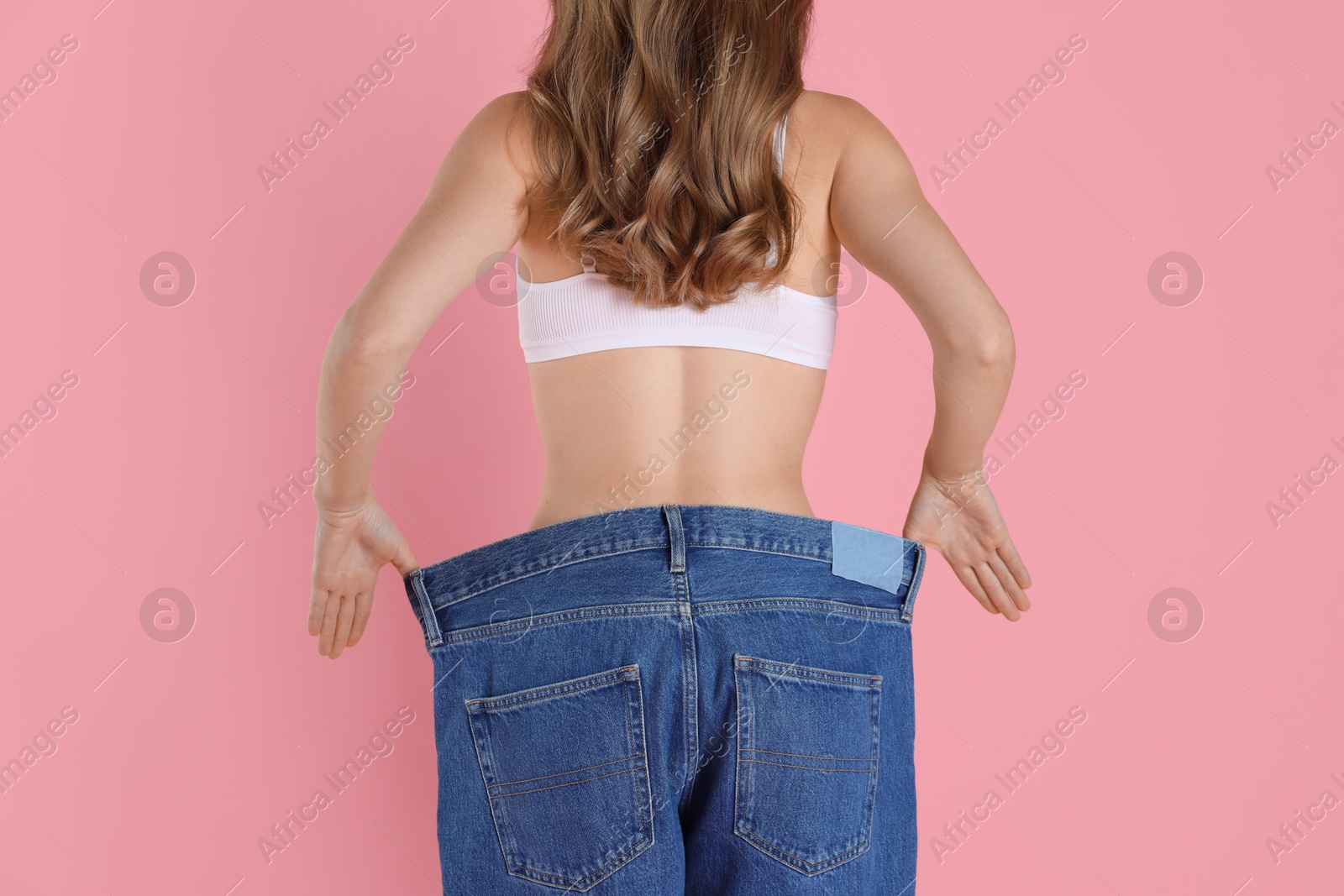 Photo of Woman in big jeans showing her slim body on pink background, closeup