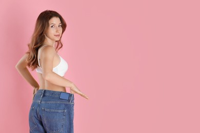 Photo of Woman in big jeans showing her slim body on pink background, space for text