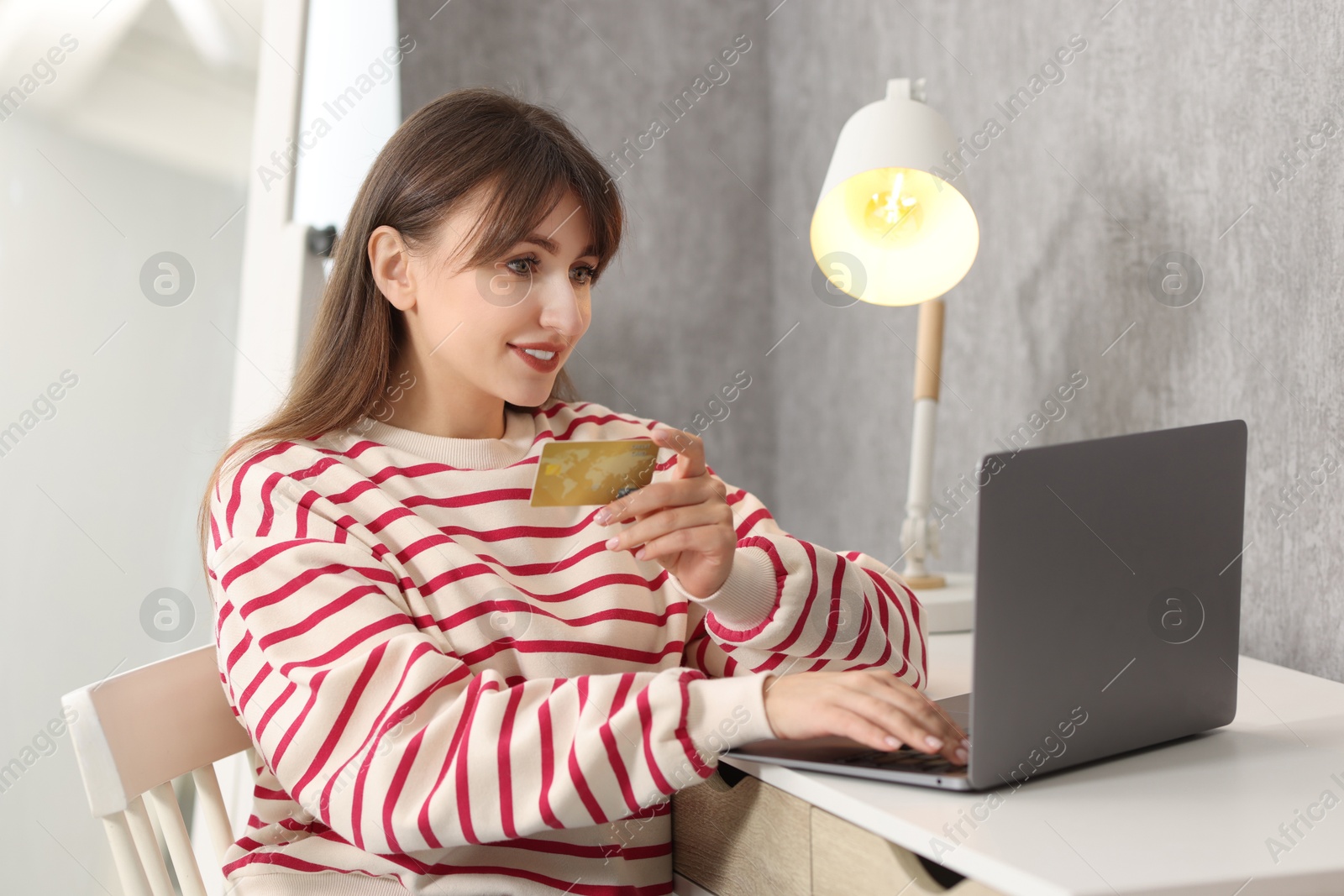 Photo of Online banking. Smiling woman with credit card and laptop paying purchase at table indoors