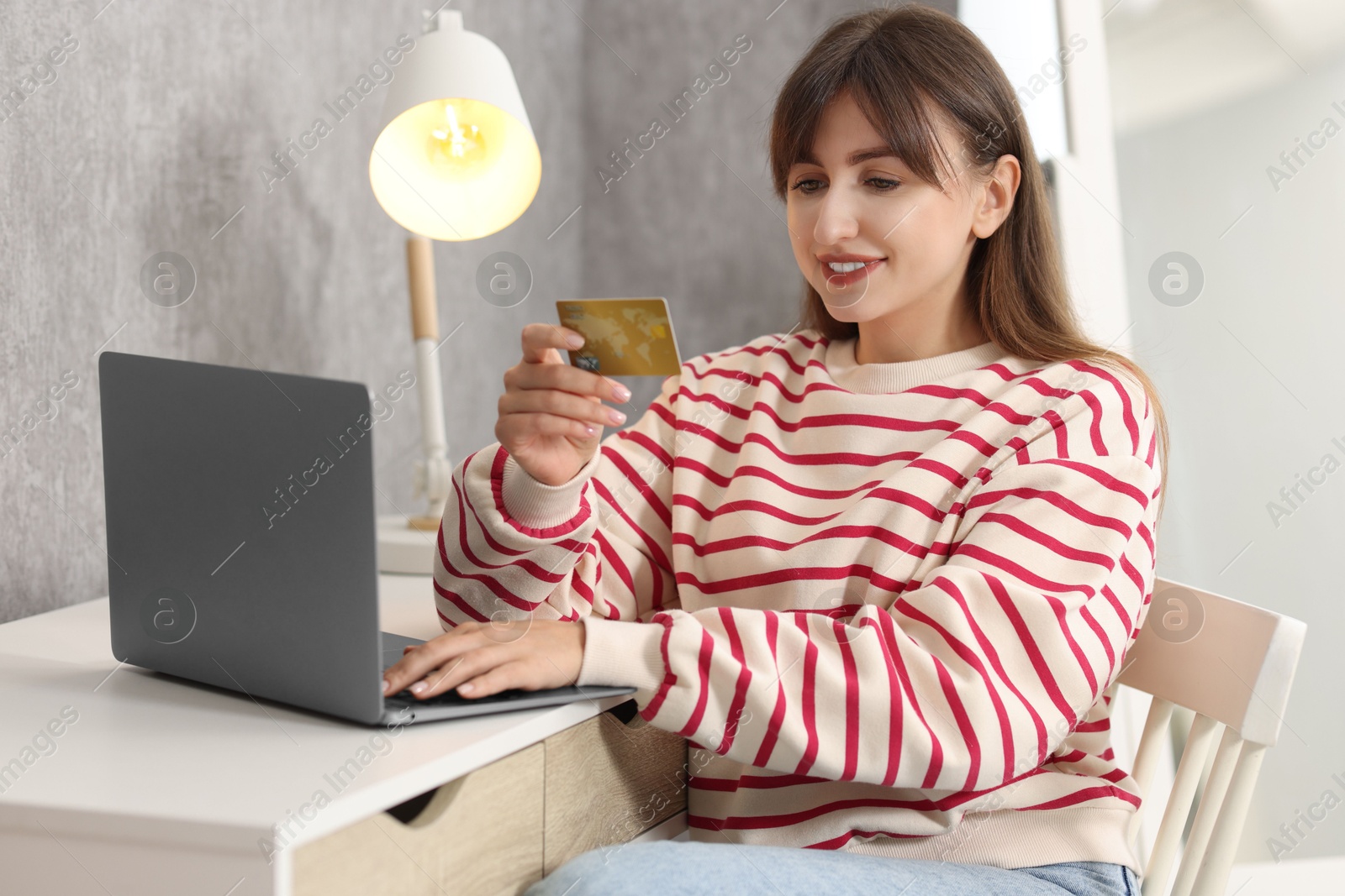 Photo of Online banking. Smiling woman with credit card and laptop paying purchase at table indoors