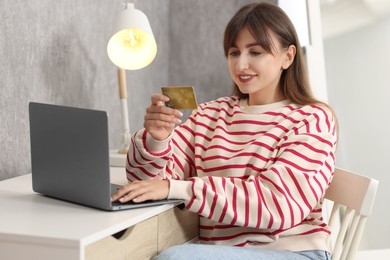 Online banking. Smiling woman with credit card and laptop paying purchase at table indoors