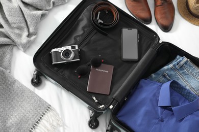 Open suitcase with traveler's belongings on bed, flat lay