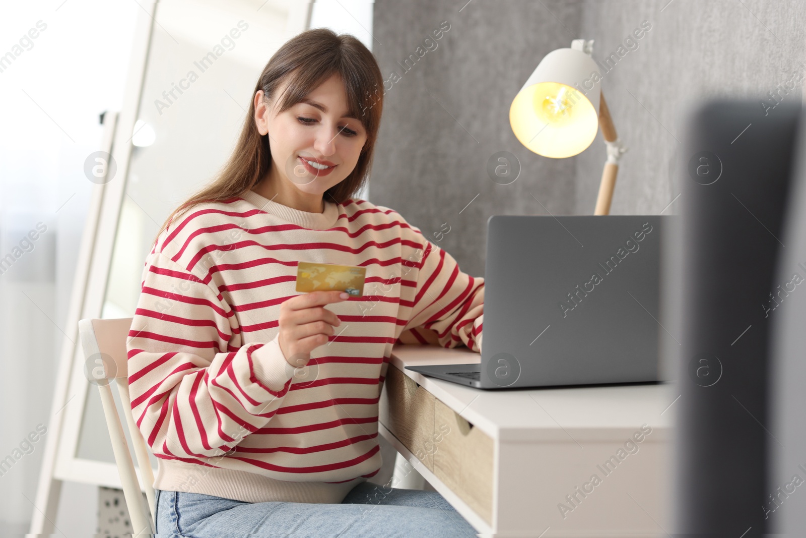 Photo of Online banking. Smiling woman with credit card and laptop paying purchase at table indoors