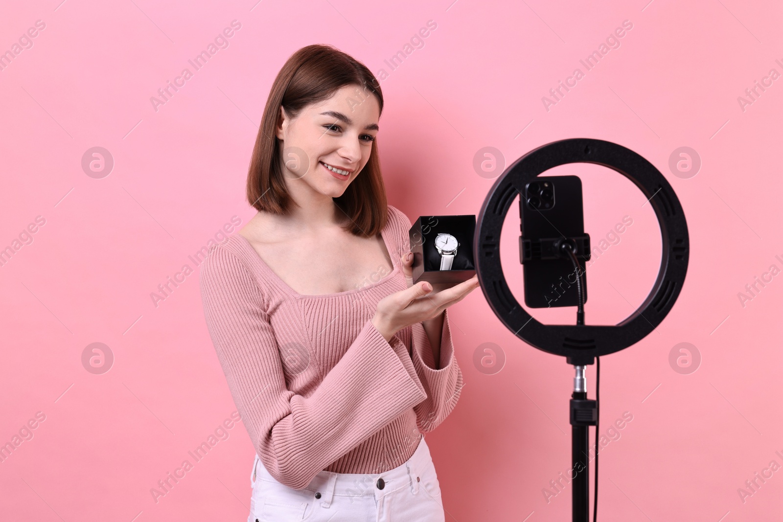 Photo of Fashion blogger reviewing watch and recording video with smartphone and ring lamp on pink background