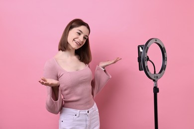 Photo of Blogger recording video with smartphone and ring lamp on pink background