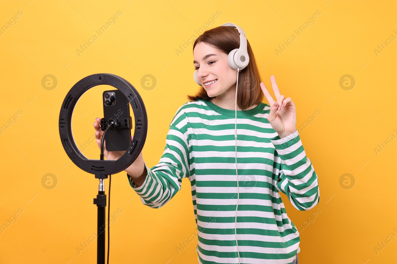 Photo of Technology blogger reviewing headphones and recording video with smartphone and ring lamp on orange background