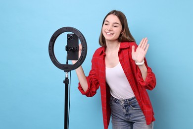 Photo of Blogger recording video with smartphone and ring lamp on light blue background