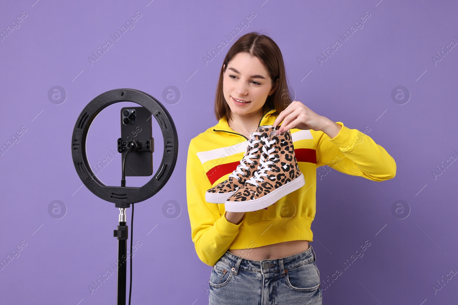 Photo of Fashion blogger reviewing sneakers and recording video with smartphone and ring lamp on purple background