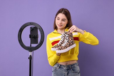 Fashion blogger reviewing sneakers and recording video with smartphone and ring lamp on purple background