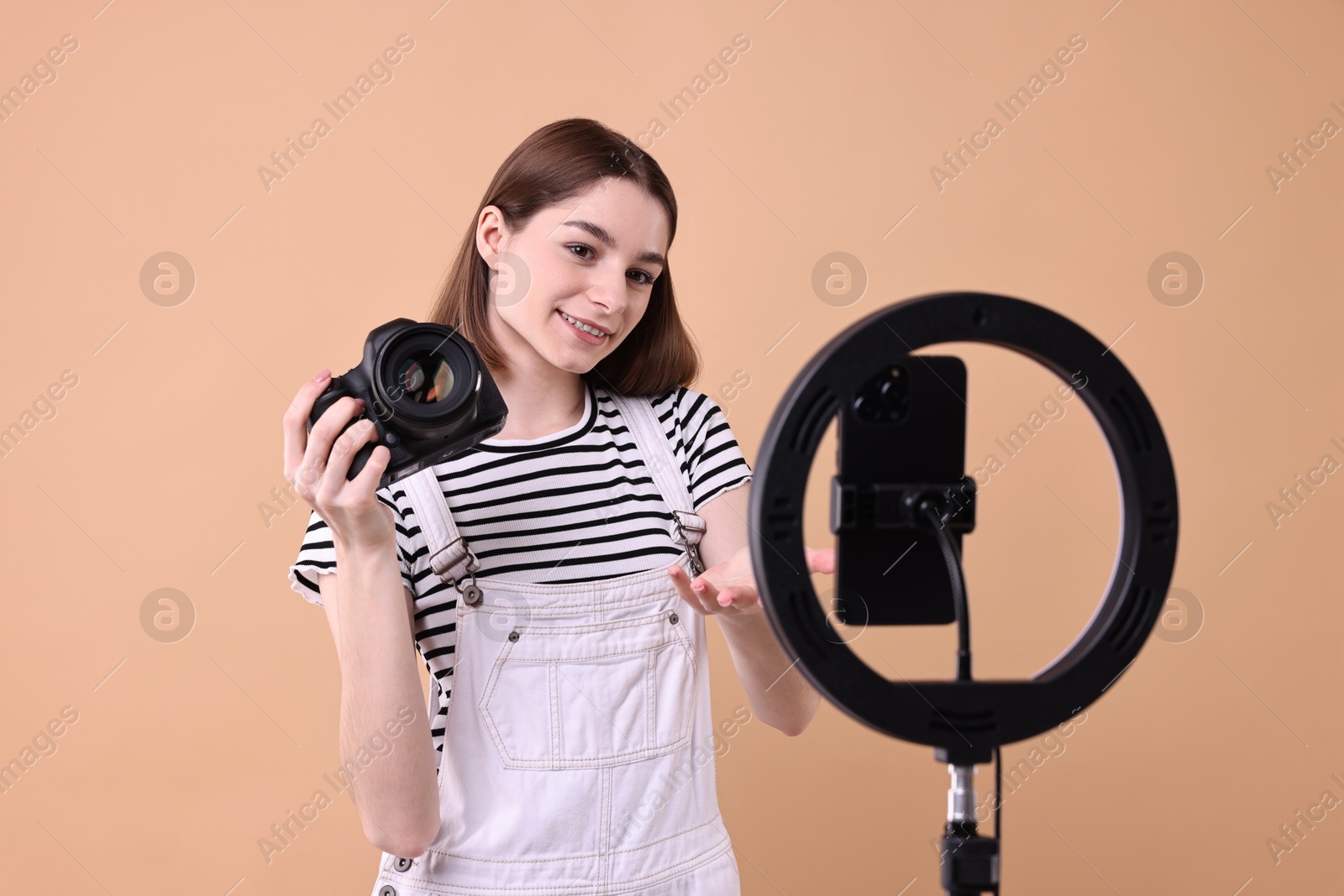 Photo of Technology blogger reviewing camera and recording video with smartphone and ring lamp on beige background