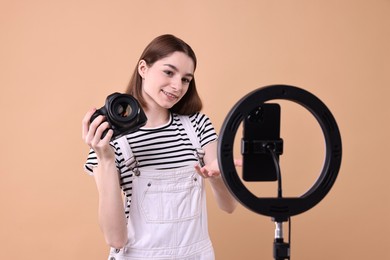 Technology blogger reviewing camera and recording video with smartphone and ring lamp on beige background