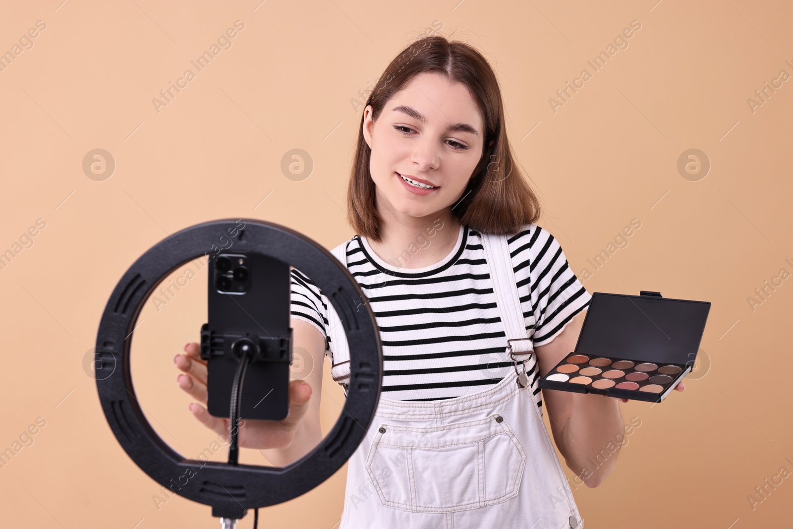 Photo of Beauty blogger reviewing eyeshadows and recording video with smartphone and ring lamp on beige background