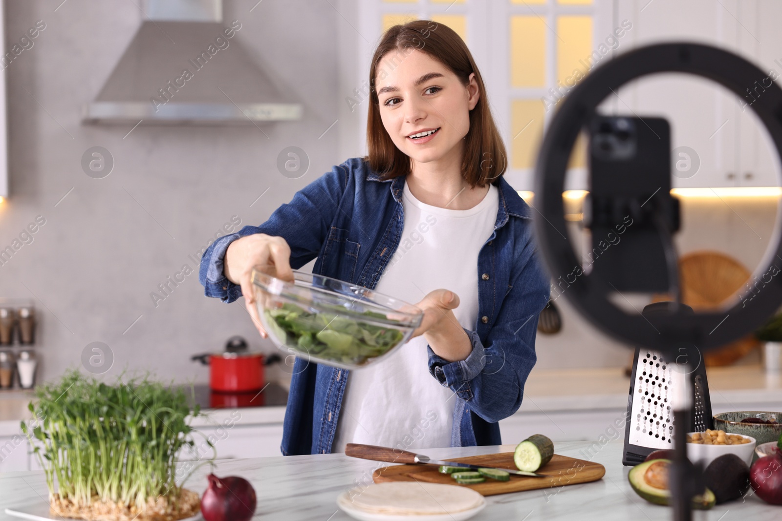 Photo of Food blogger cooking while recording video with smartphone and ring lamp in kitchen