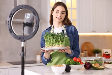 Food blogger cooking while recording video with smartphone and ring lamp in kitchen