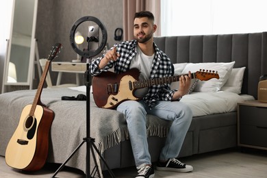 Photo of Music blogger recording guitar lesson with smartphone and ring lamp at home