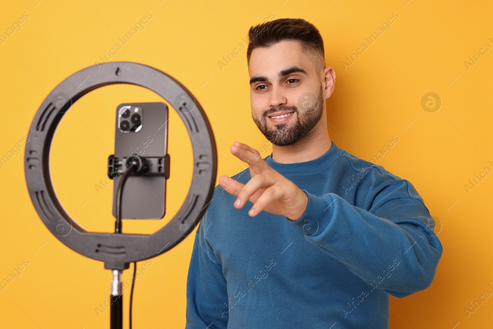 Photo of Blogger recording video with smartphone and ring lamp on orange background