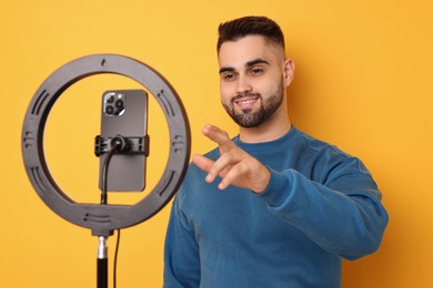 Photo of Blogger recording video with smartphone and ring lamp on orange background