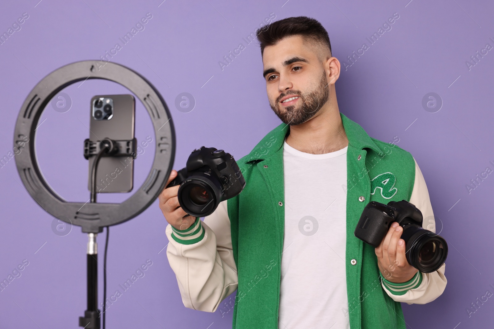 Photo of Technology blogger reviewing cameras and recording video with smartphone and ring lamp on purple background