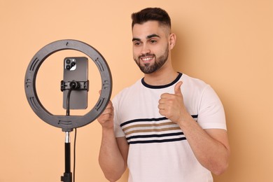 Blogger recording video with smartphone and ring lamp on beige background