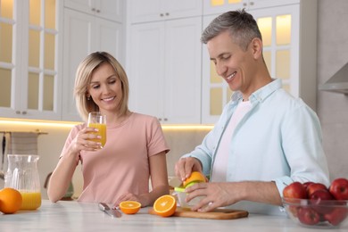 Photo of Happy couple with juicer and fresh products making juice at white marble table in kitchen