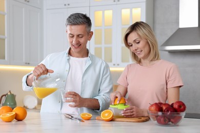 Happy couple with juicer and fresh products making juice at white marble table in kitchen