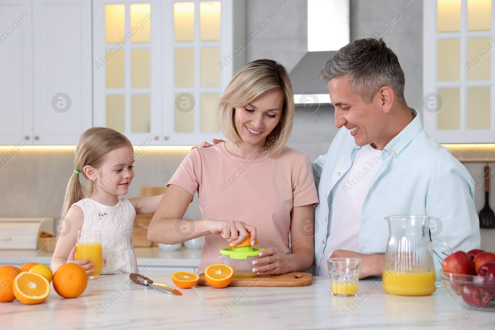 Photo of Happy family making juice at white marble table in kitchen