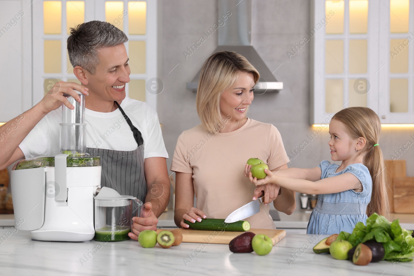 Photo of Happy family with juicer and fresh products making drink at white marble table in kitchen