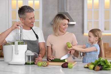 Photo of Happy family with juicer and fresh products making drink at white marble table in kitchen