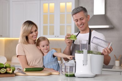 Photo of Happy family with juicer and fresh products making drink at white marble table in kitchen