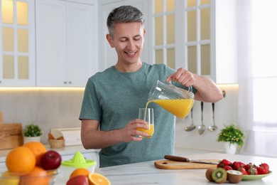 Photo of Smiling man pouring fresh orange juice into glass at white marble table in kitchen