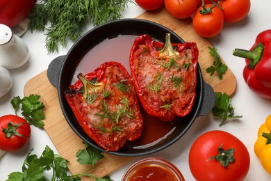 Photo of Tasty stuffed peppers in dish and ingredients on white table, flat lay