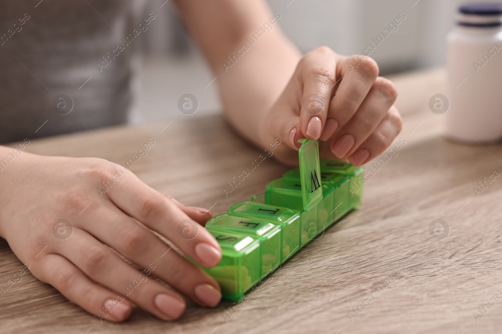 Photo of Woman with pills and organizer at wooden table, closeup