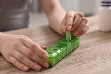 Woman with pills and organizer at wooden table, closeup